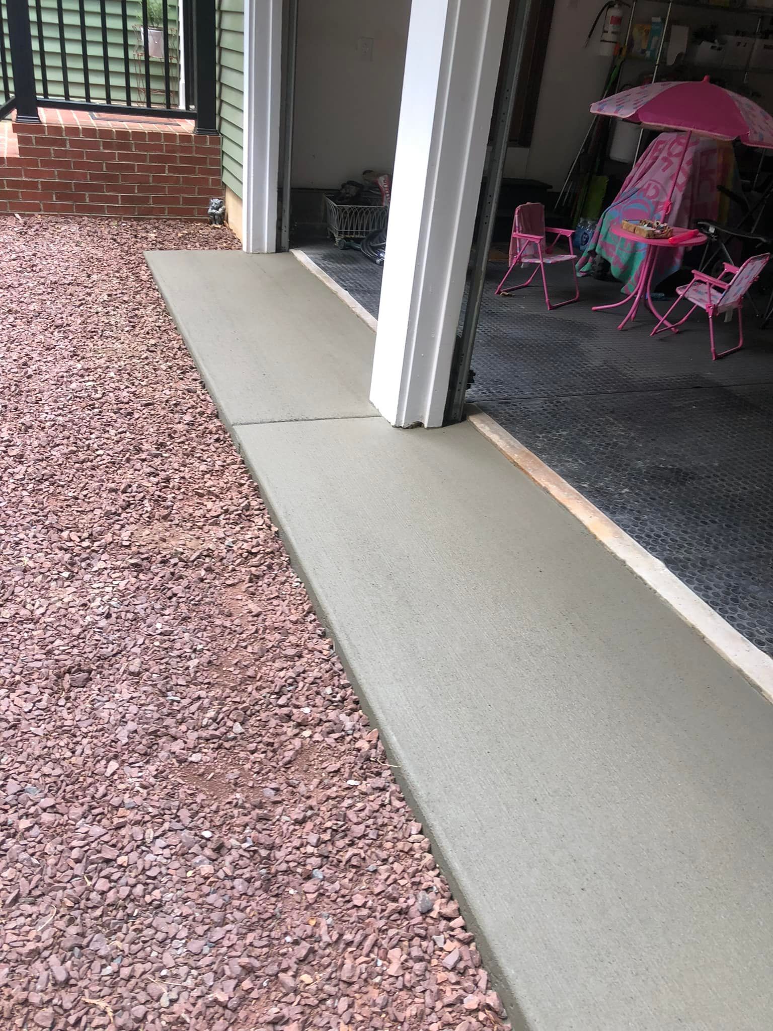 A concrete walkway leading to a garage with a pink table and chairs.