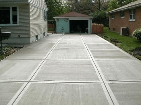 A concrete driveway leading to a garage next to a house.