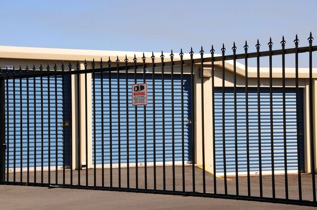 Black metal gate in front of a white garage door with a small warning sign.