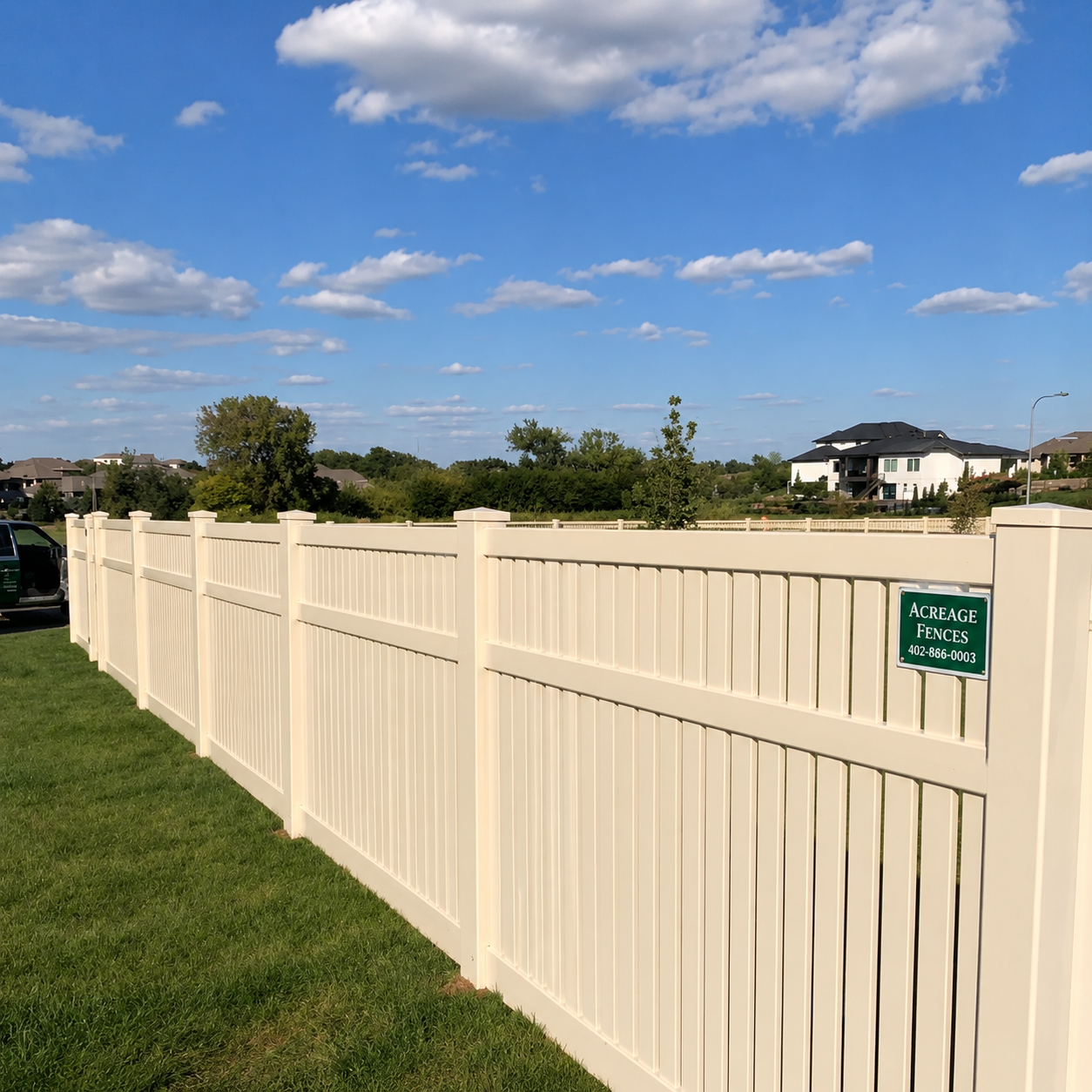Cream-colored fence along a grassy field under a blue sky with clouds