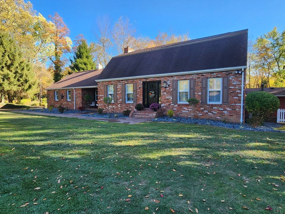 Brick ranch house with brown roof and shutters, surrounded by green lawn and fall foliage.