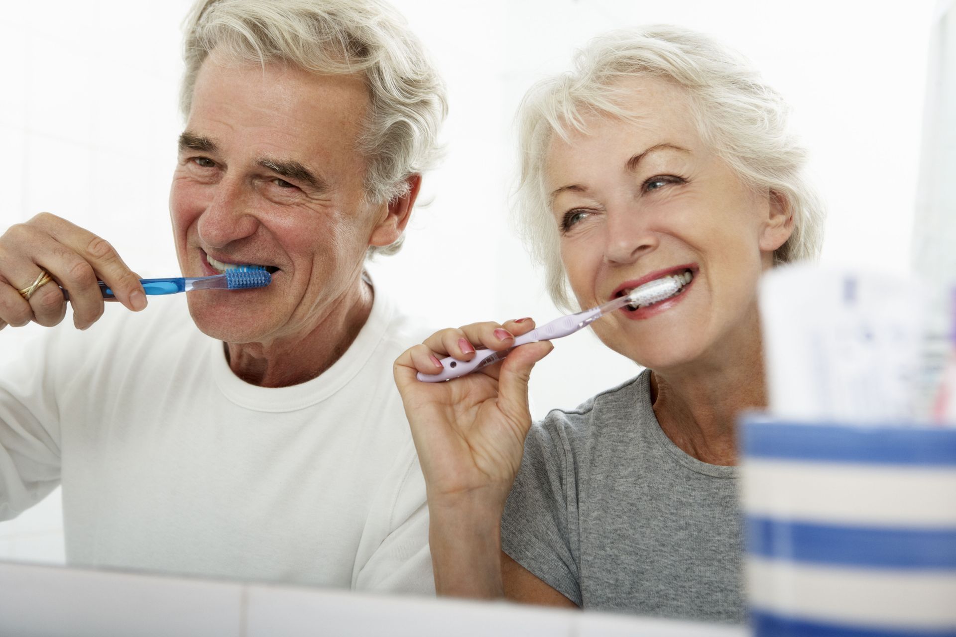 Older couple brushing teeth in a bathroom, smiling.