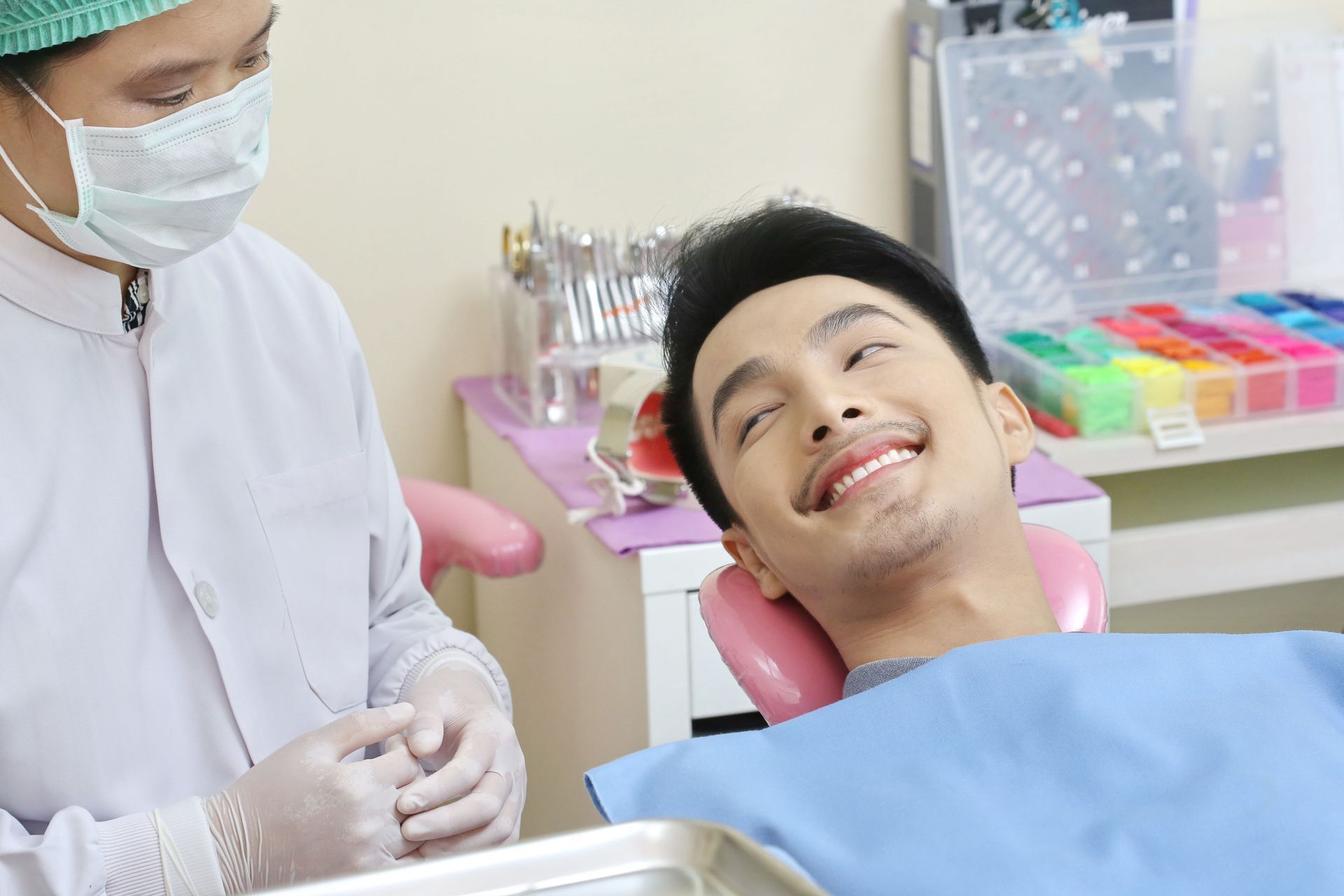 Dentist wearing a mask examining a smiling patient in a dental chair.