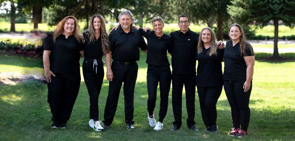 Seven people in black clothing stand shoulder to shoulder on a grassy lawn.