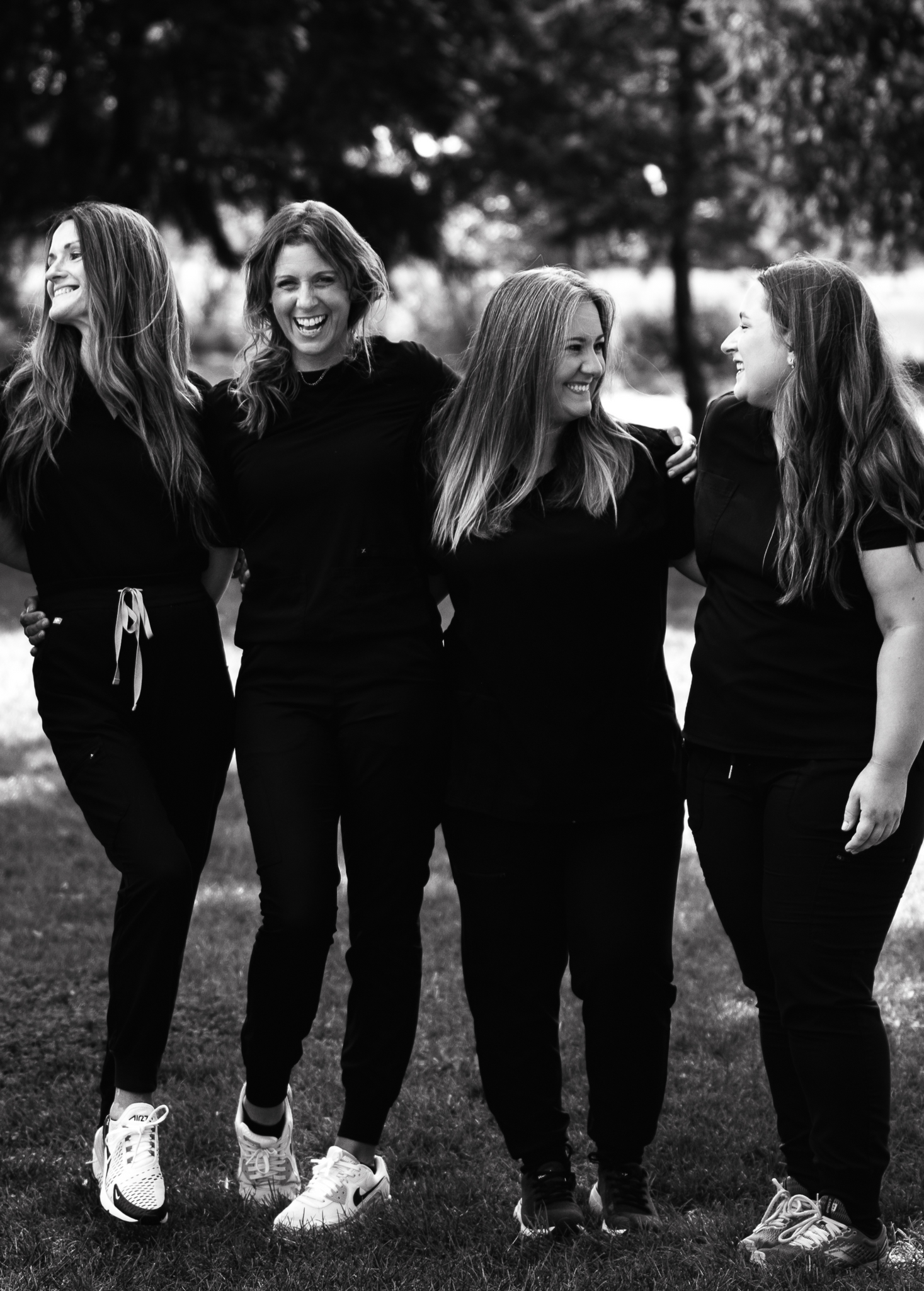 Five people in black clothing stand arm-in-arm outside, smiling.