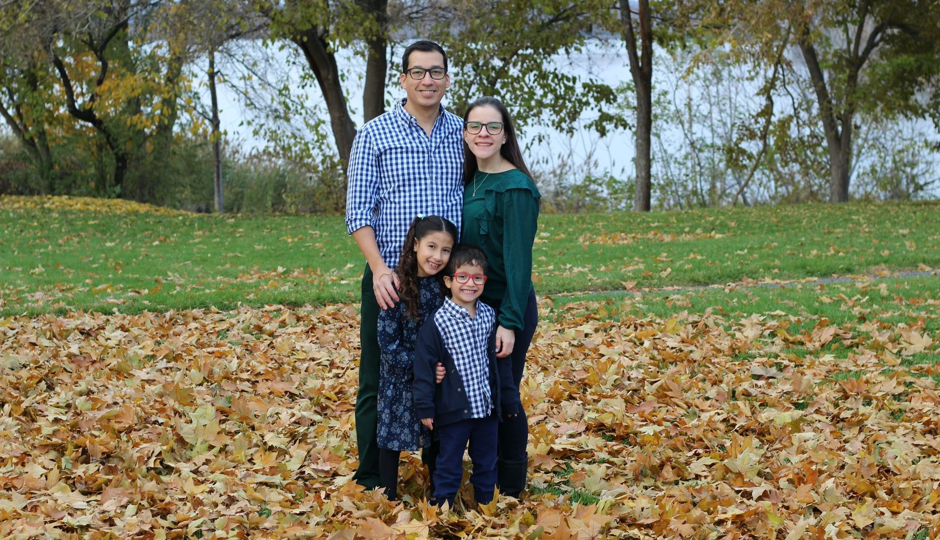 Family of four posing on a bed of fall leaves; man in blue shirt, woman in green, two children.
