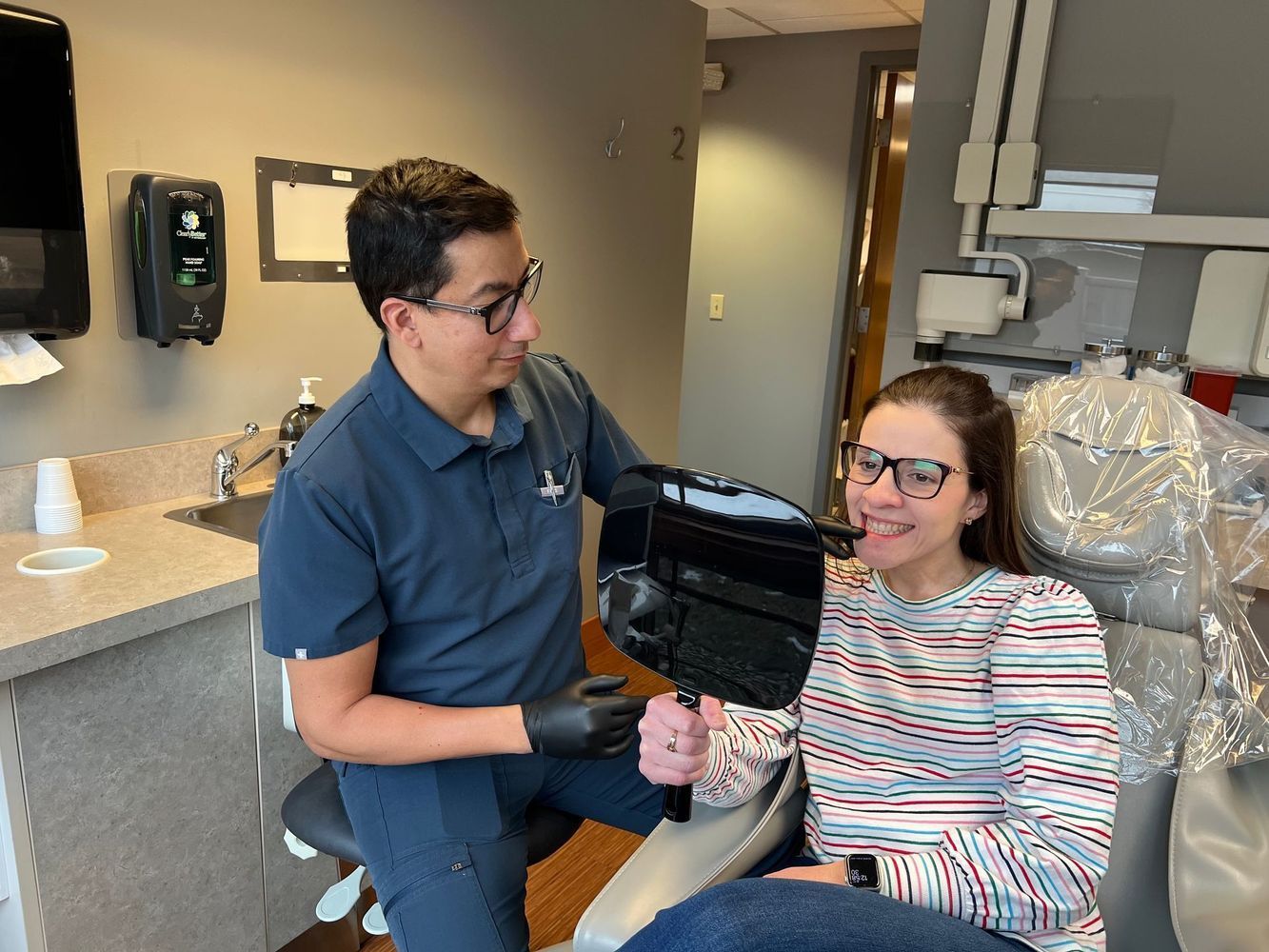 Dentist showing patient her teeth in a mirror. They are in a dental office.