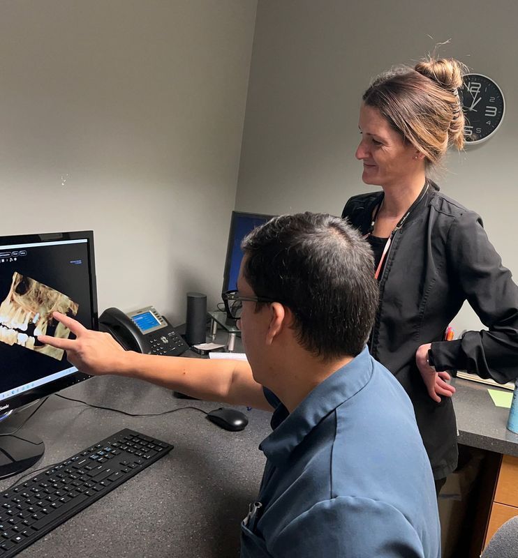 Two people examining dental x-ray on a monitor. Man points at screen, woman observes, indoors.
