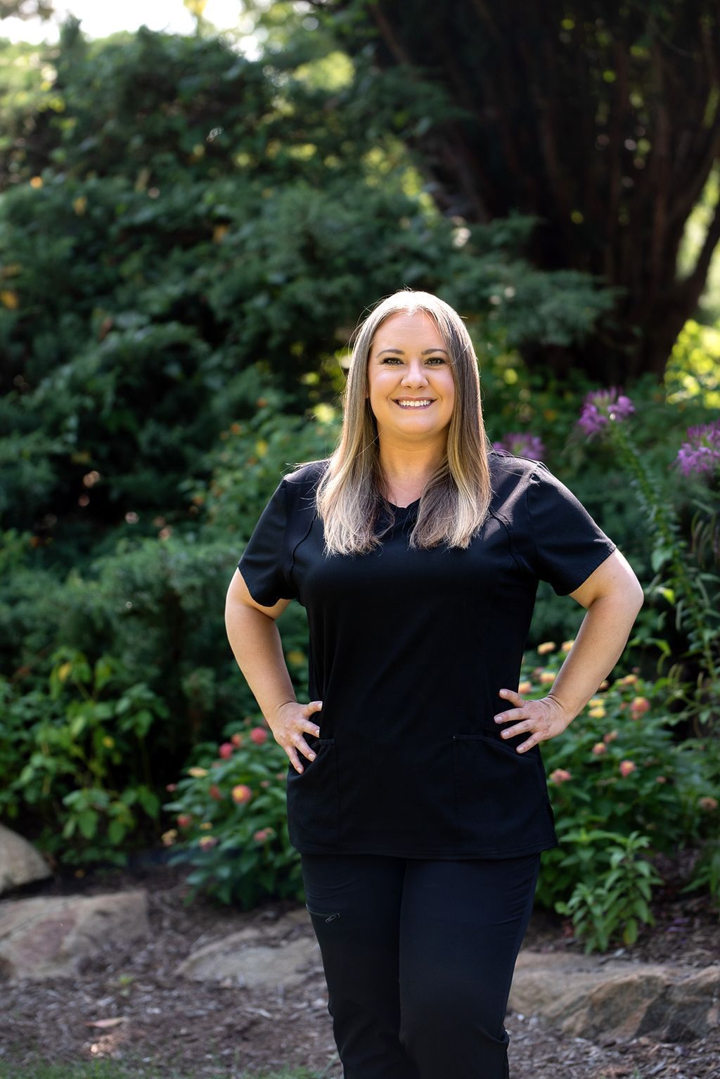 Woman with hands on hips in black scrubs poses outdoors.