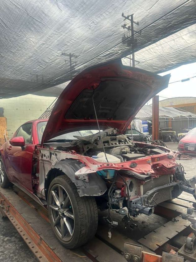 Damaged red SUV with open hood and missing front end on a tow truck under a canopy.