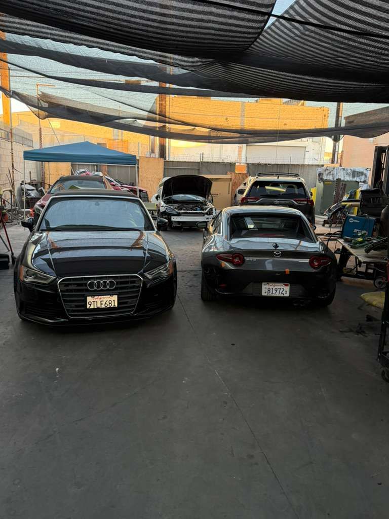 Two black cars parked under a shaded canopy in a parking lot
