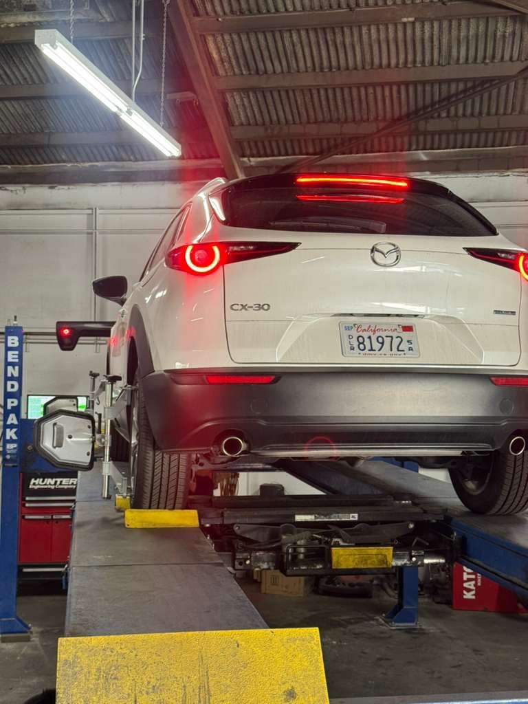 White SUV on a mechanic’s lift in an auto repair shop, viewed from the rear with brake lights on.