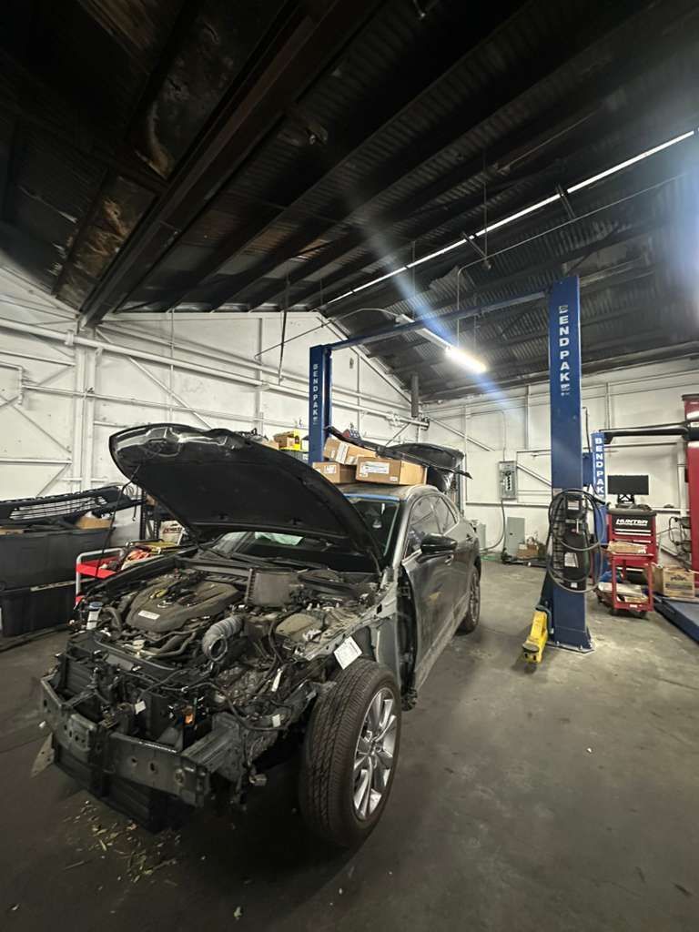 Damaged SUV in an auto repair shop with hood open and front-end crash damage