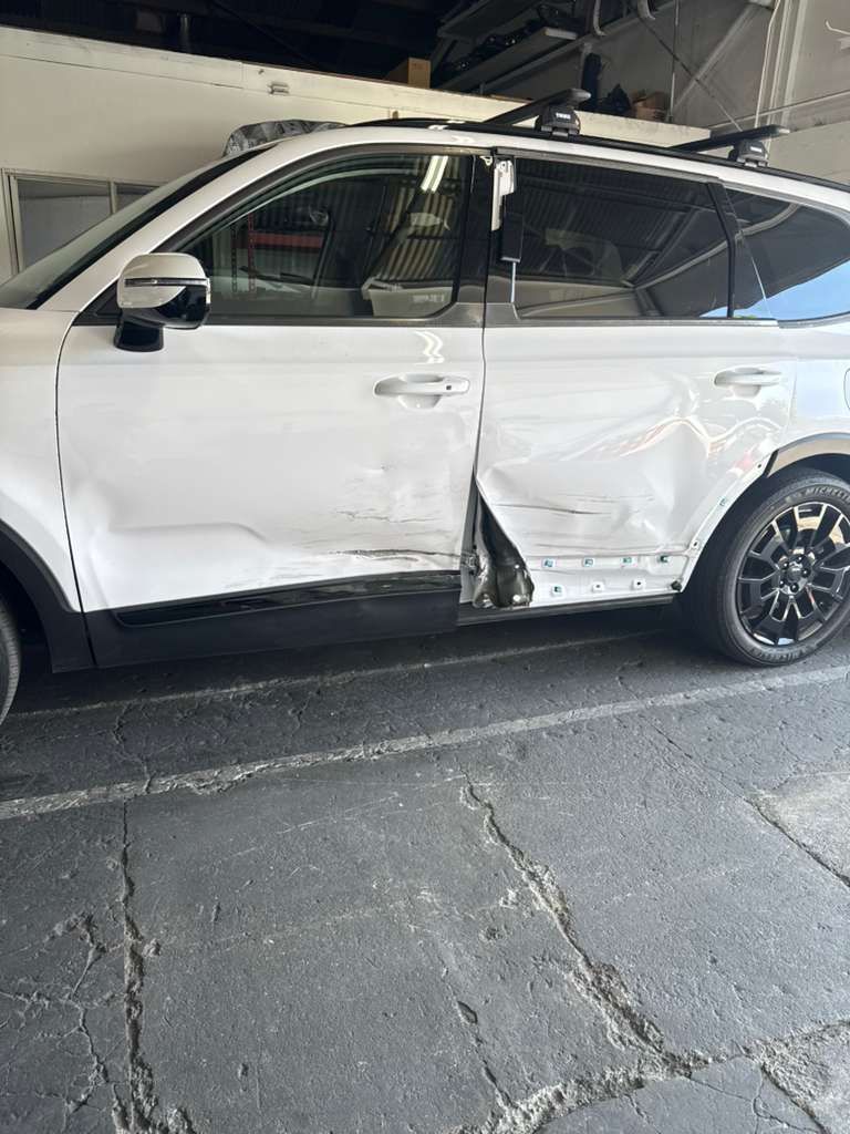 White SUV with heavy side damage and a crumpled rear door in a parking garage.