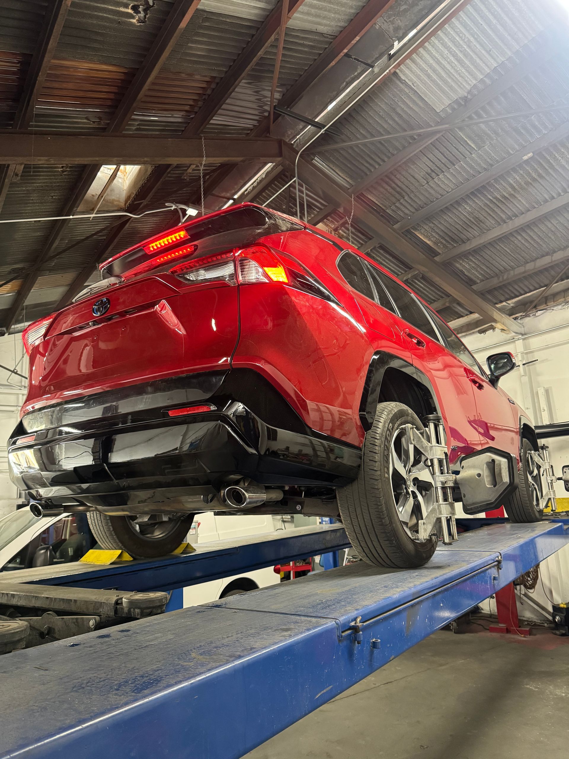 Red SUV on a car lift in an auto repair shop, viewed from the rear underside.