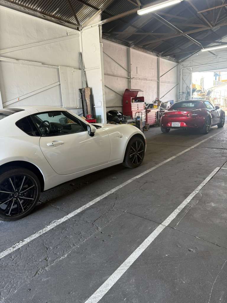 Two sports cars parked inside a warehouse, a white coupe in front and a red car behind.