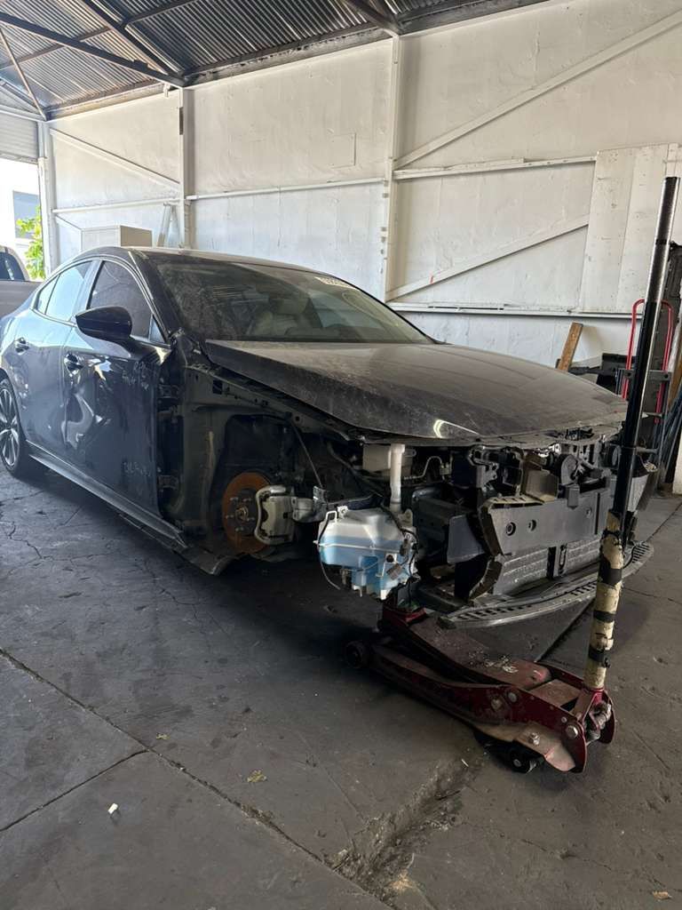 Damaged black sedan in a garage, front end removed and sitting on a jack stand.
