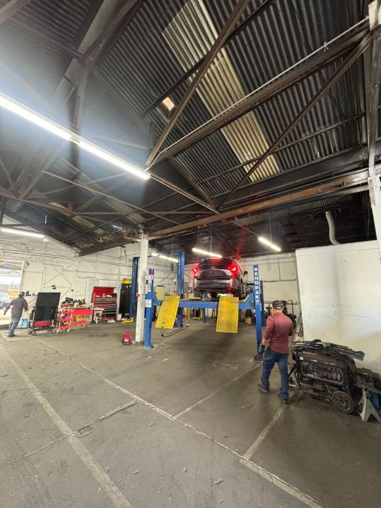 Auto repair shop interior with a lift, tools, and two workers near a car under the roof trusses