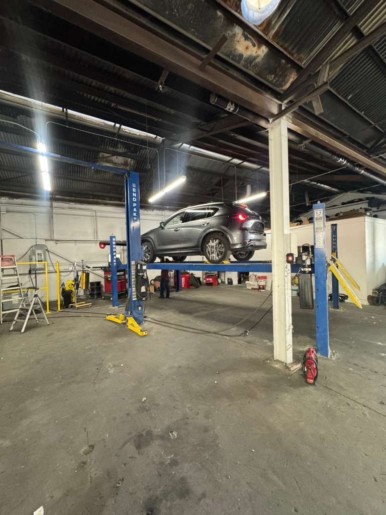 Silver car on a blue hydraulic lift in an auto repair shop with industrial ceiling and equipment