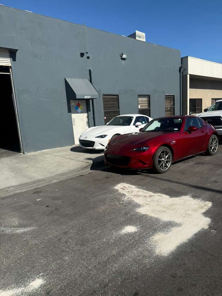Red sedan and white coupe parked outside a gray industrial building on a sunny day