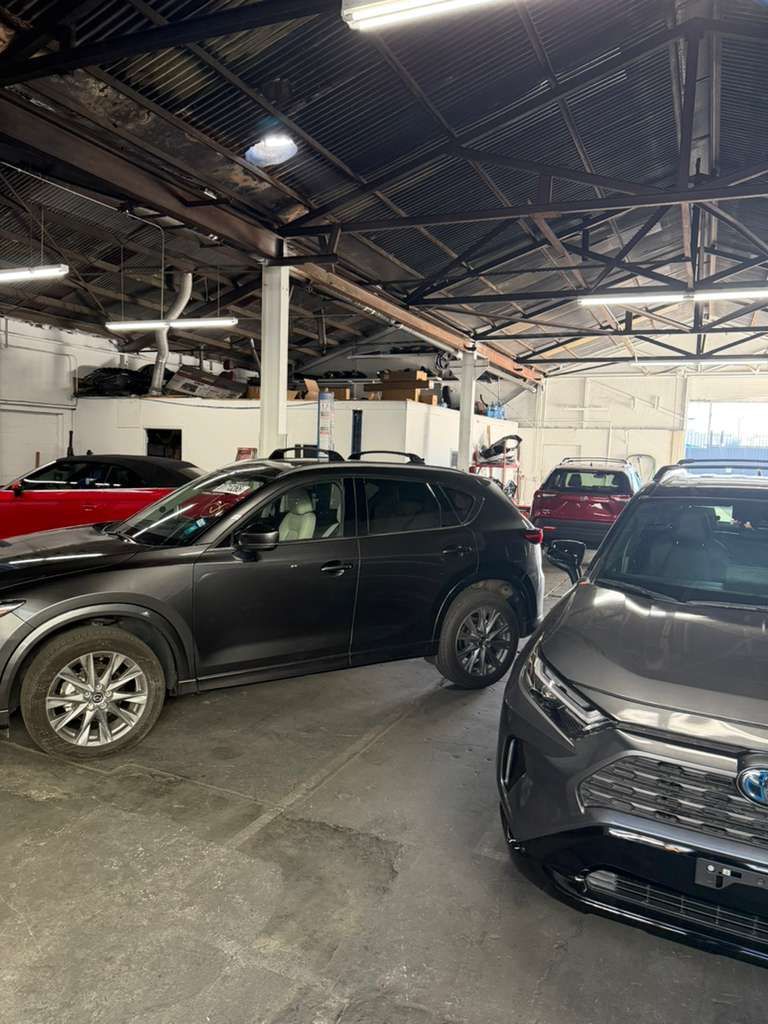Cars parked inside an auto shop with a high metal roof and bright daylight coming through the open entrance.