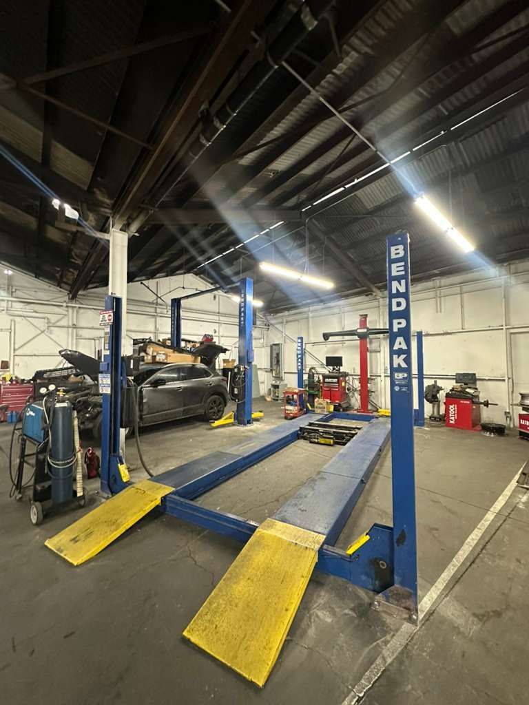 Auto repair shop with blue BendPak car lift and yellow ramps under a high industrial ceiling