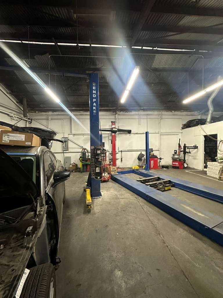 Auto repair shop with a vehicle lift, a black car, and fluorescent lights overhead