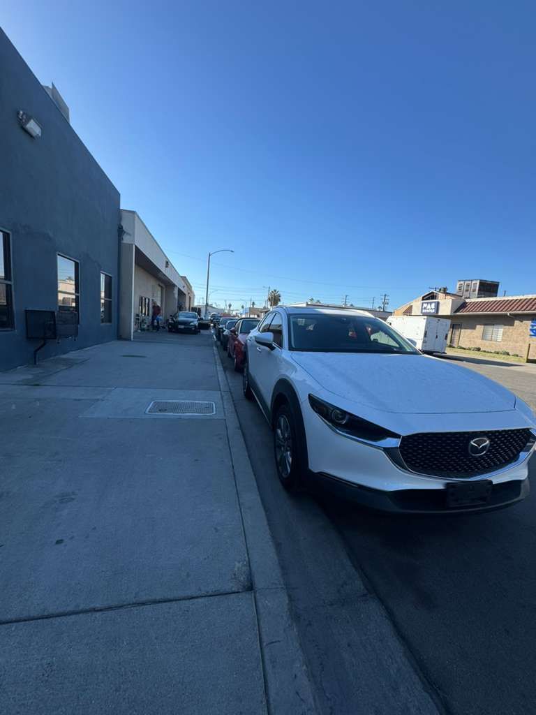 White car parked on a sunny street beside a gray building under a clear blue sky
