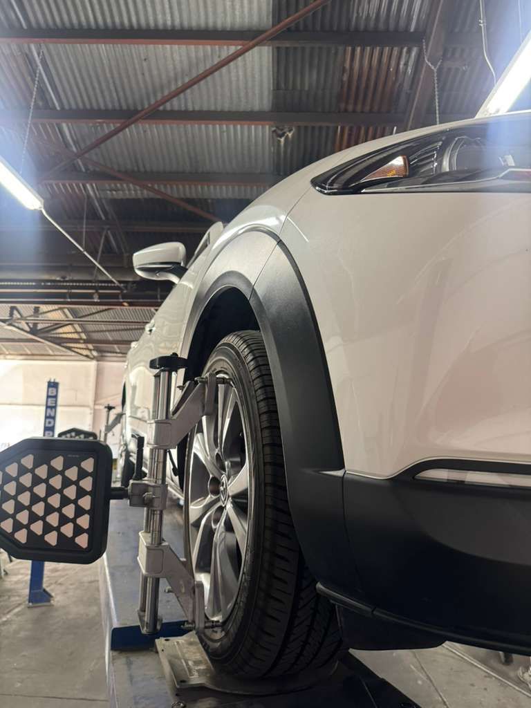 White car on a wheel alignment lift in an auto shop, viewed from the front side.