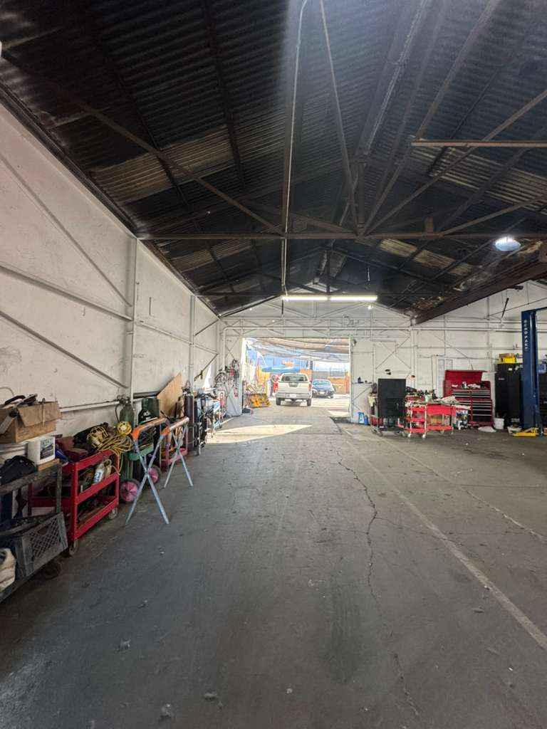 Empty industrial warehouse with high ceiling, scattered tools and equipment, and bright daylight at the open entrance