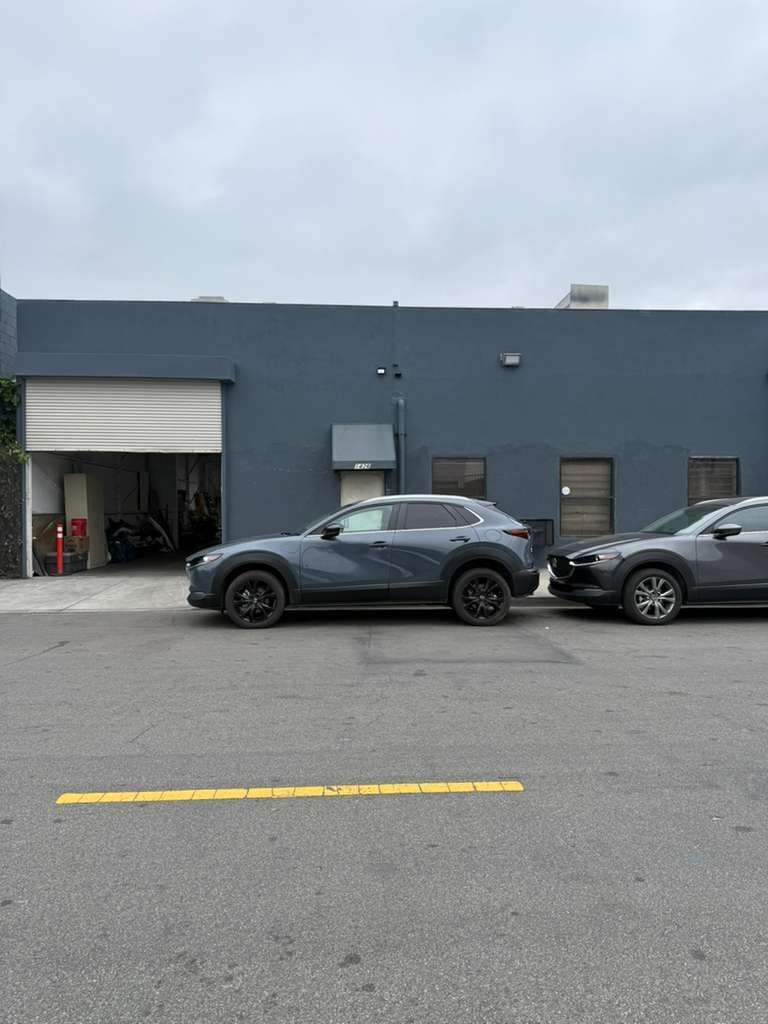 Two parked cars outside a gray industrial building with an open garage door.