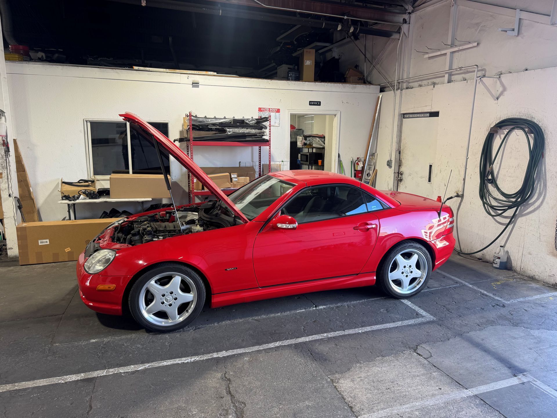 Red sports coupe in a garage with its hood open, showing the engine.