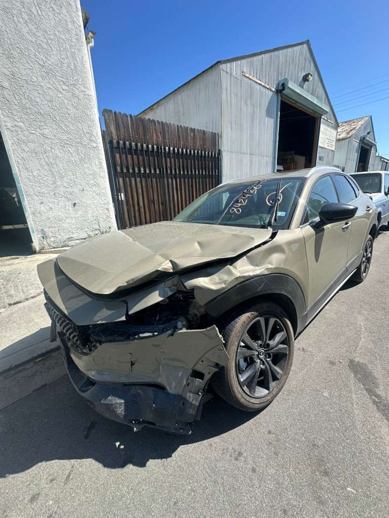 Damaged gray sedan with crumpled hood and front end on a street beside industrial buildings