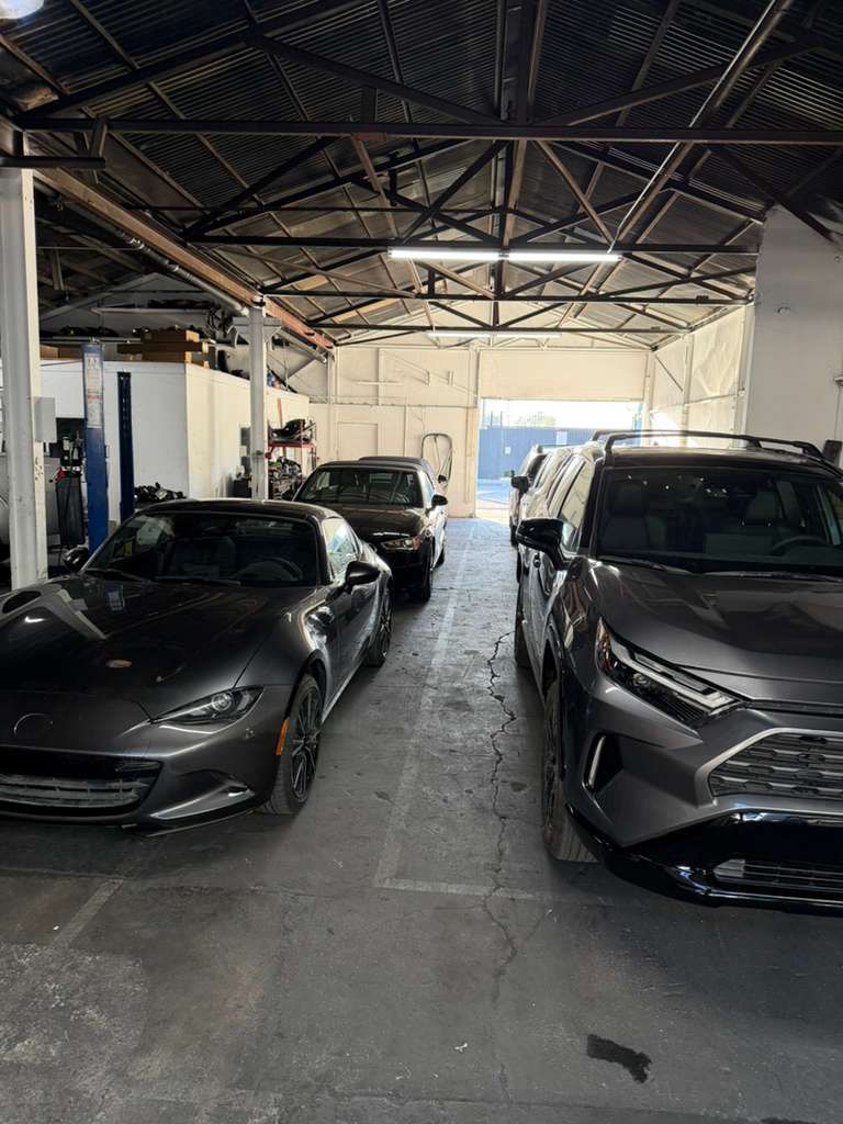 Two gray cars parked inside a warehouse garage with a metal roof and open doorway.