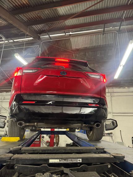 Red car lifted on a hydraulic auto shop lift in a garage, rear view visible