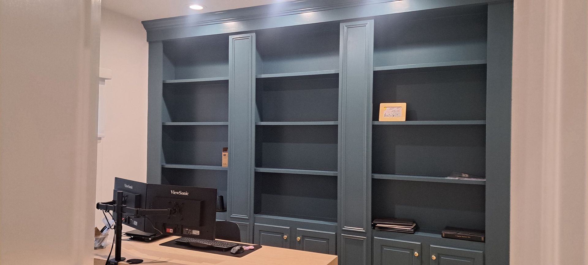 Modern office with built-in dark shelves, a desk, and computer monitors under recessed lighting