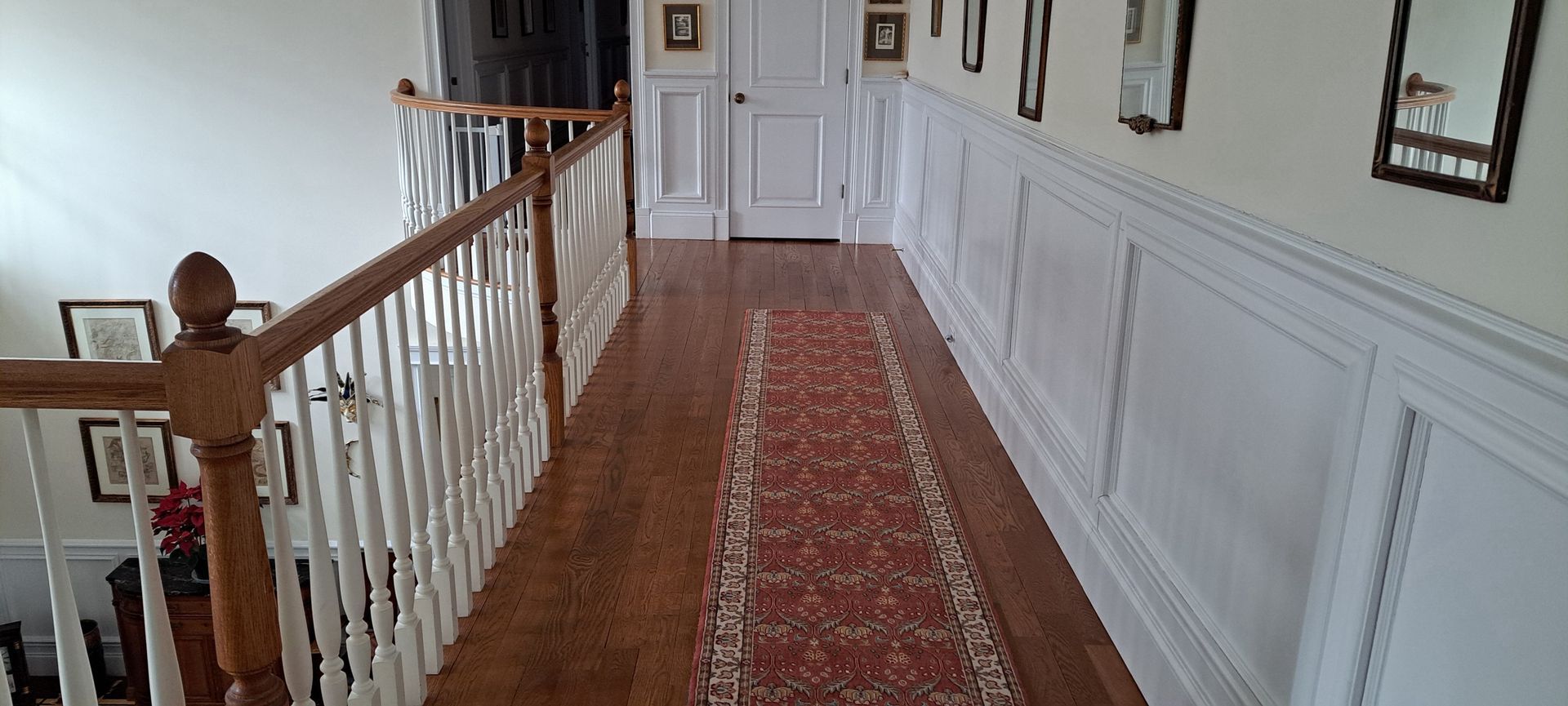 Narrow hallway with white paneled walls, red runner carpet, and wooden railing