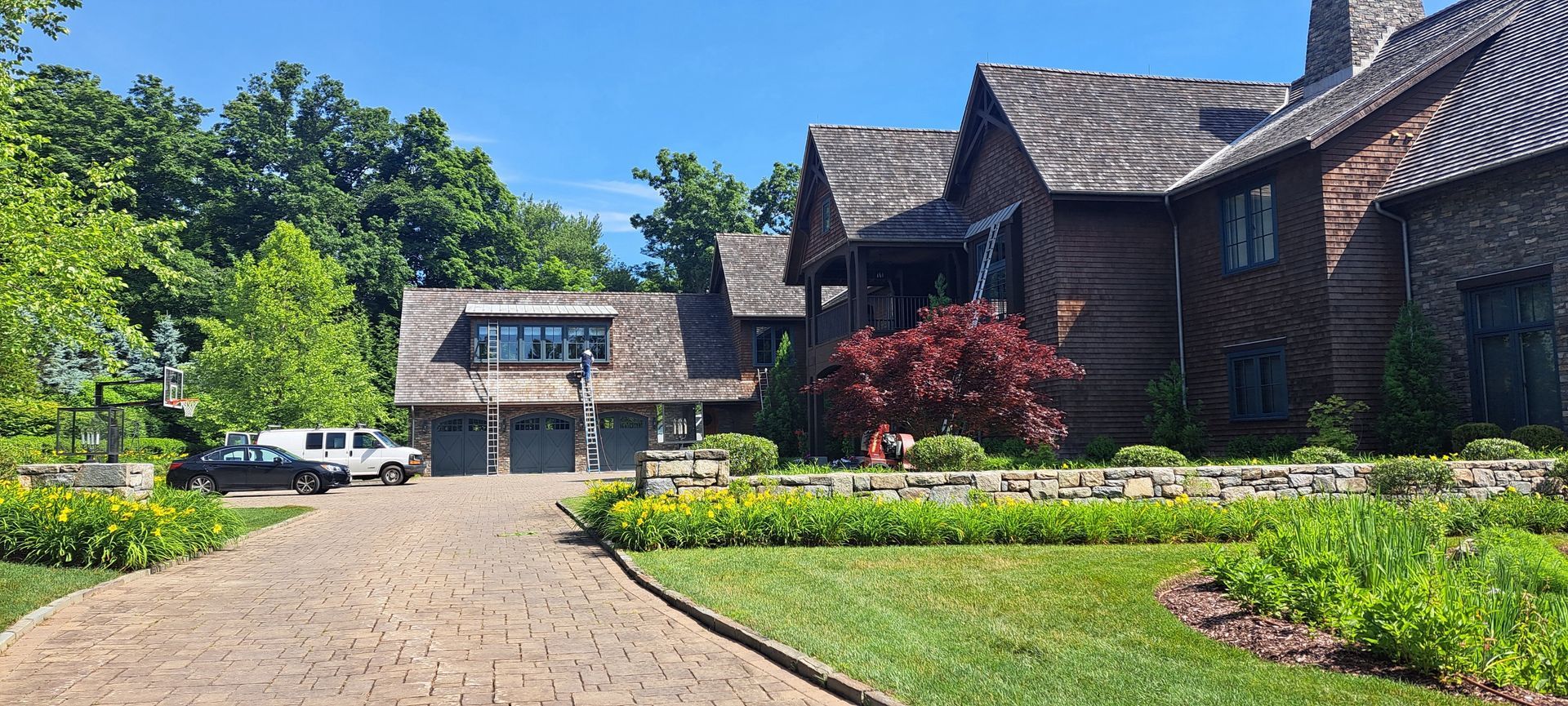 Large stone house with a curved driveway, green lawn, and blue sky on a sunny day