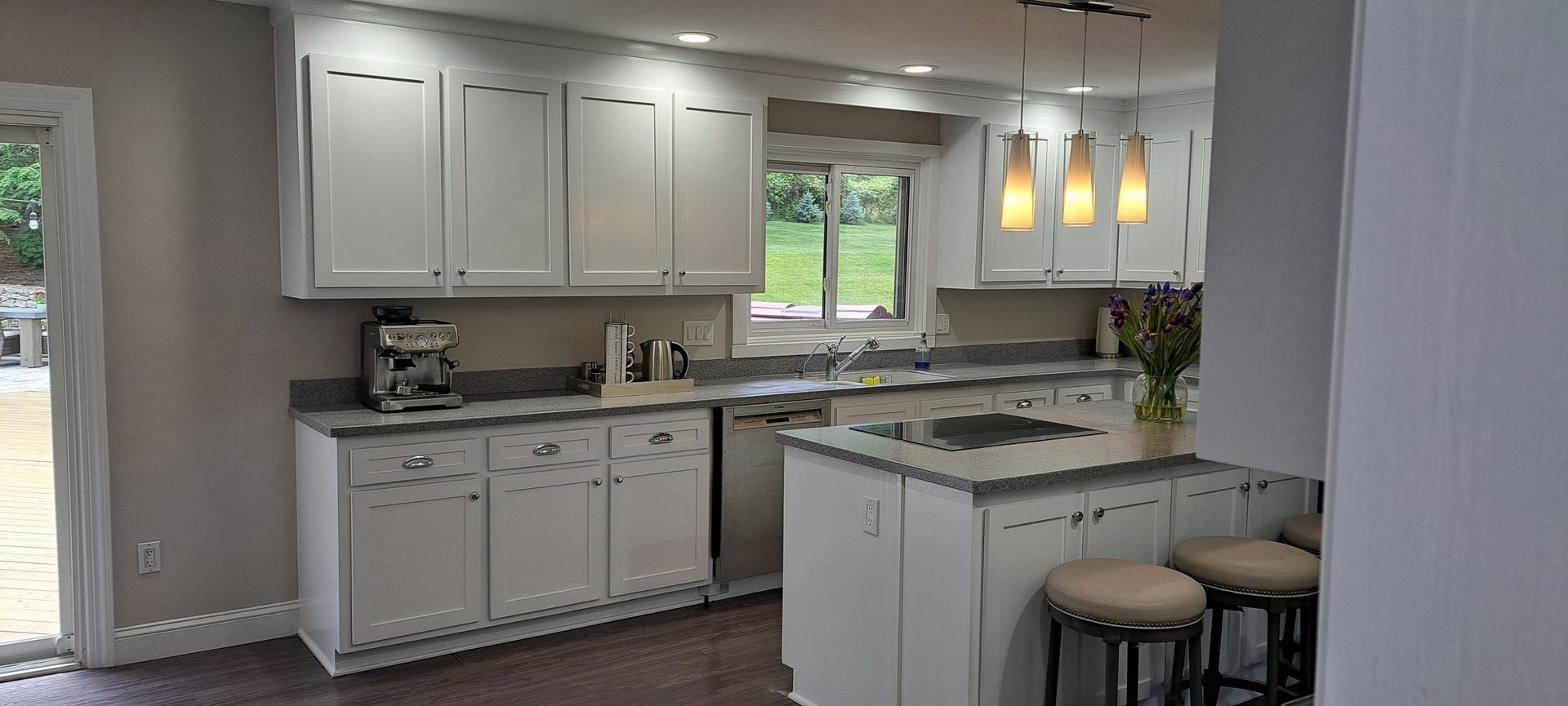 Bright kitchen with white cabinets, gray counters, window, sink, and three pendant lights over a peninsula.
