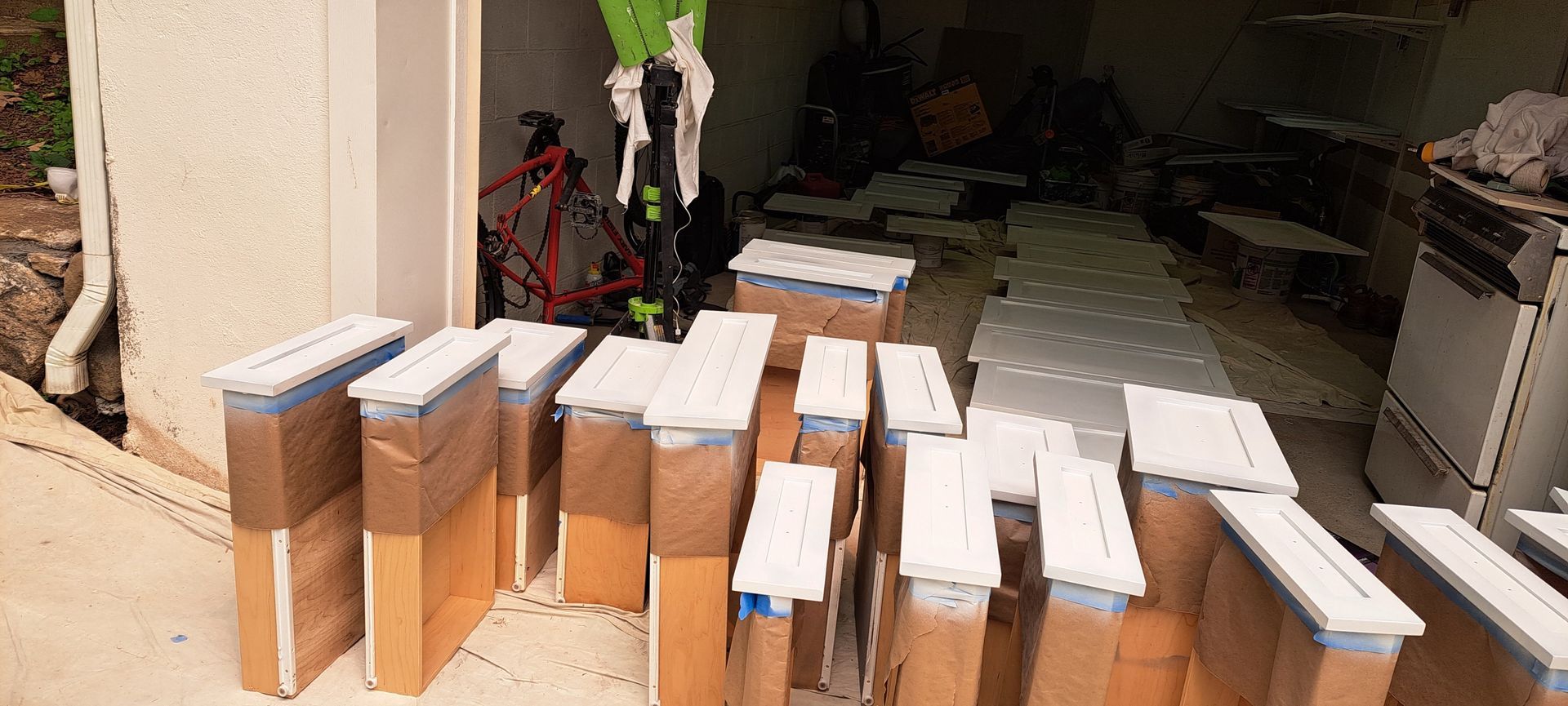Cardboard boxes lined up outside a garage, with white foam boards on top and a bicycle in the background
