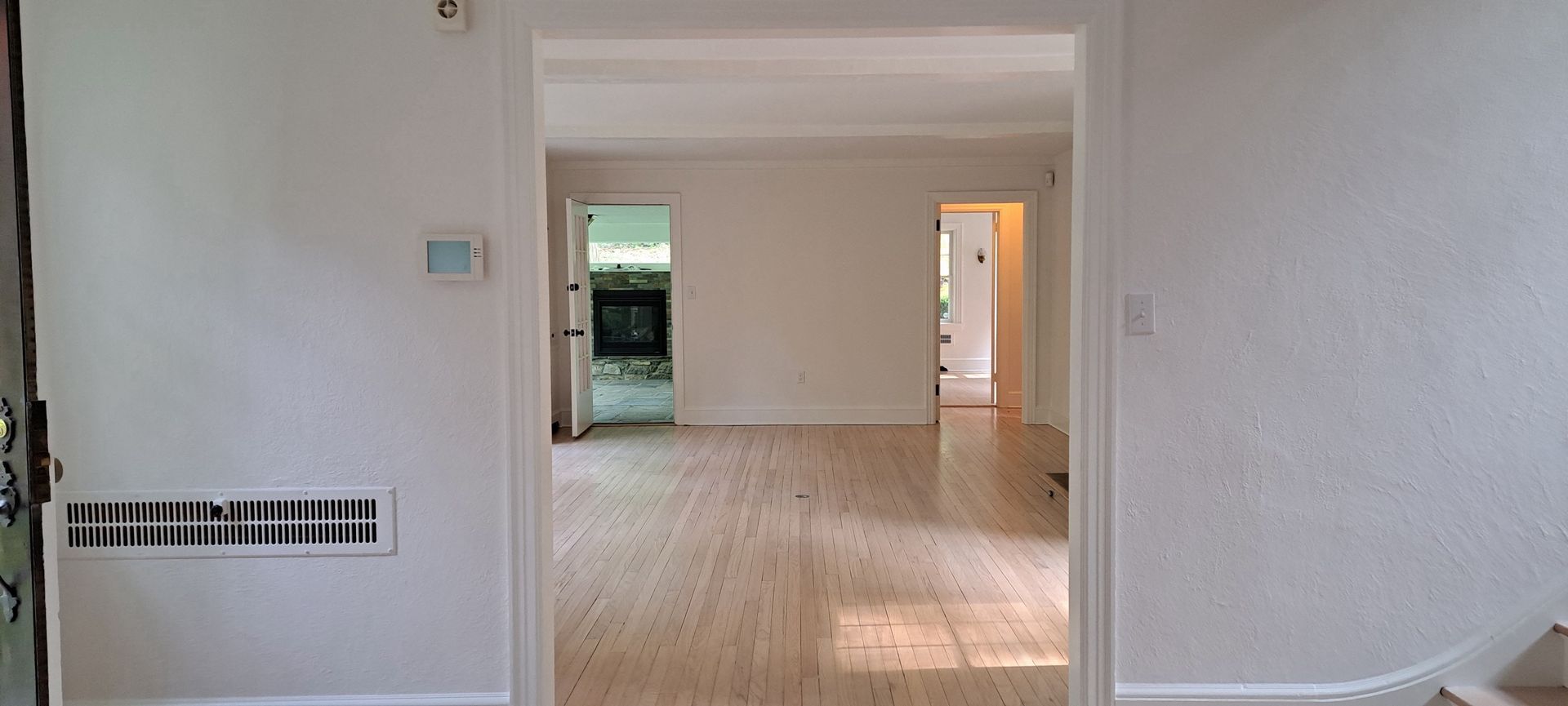 Interior hallway with white walls, wood floors, and a short step up to a brighter room beyond