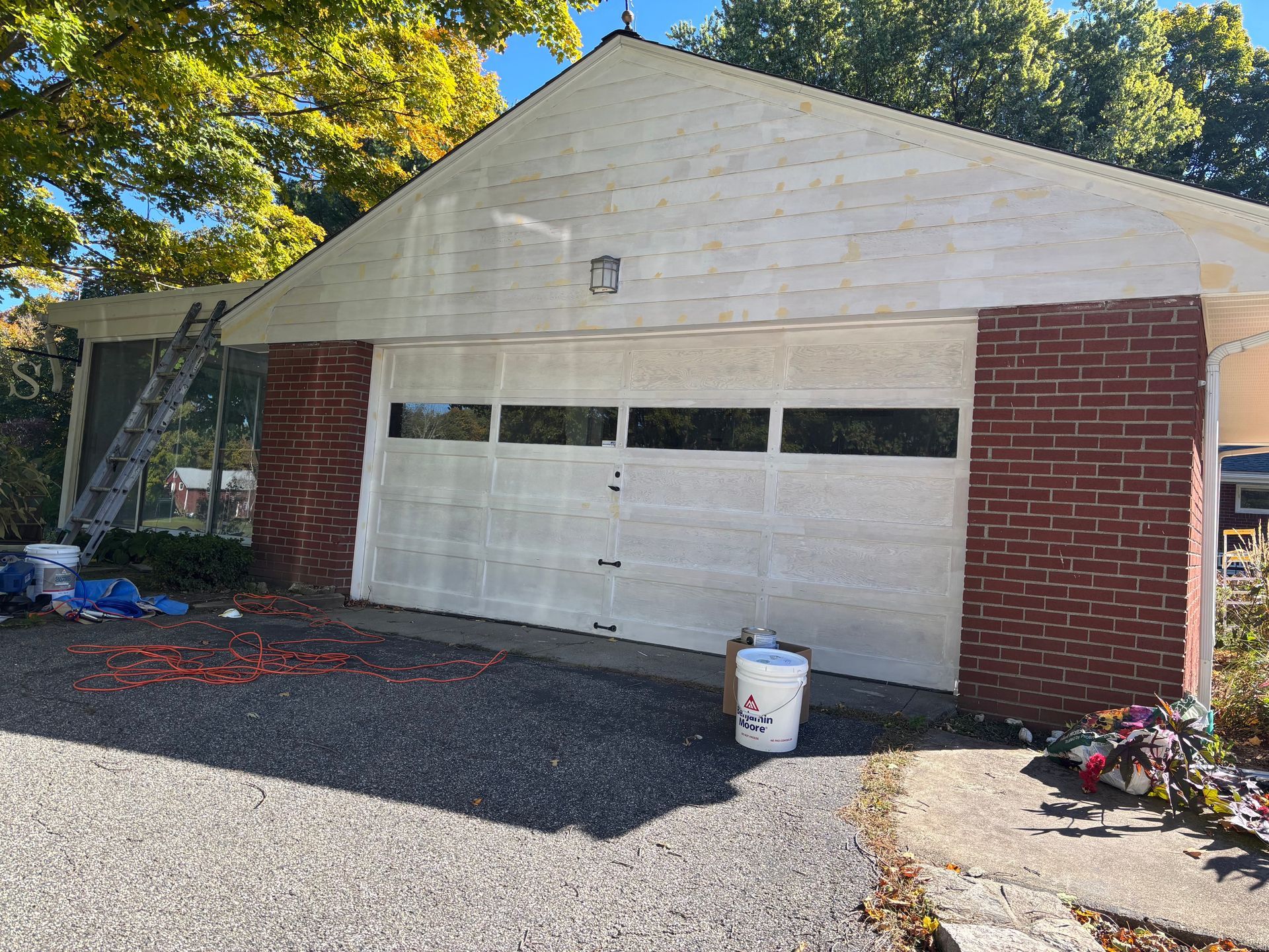 White garage with red brick sides and a driveway, seen in bright sunlight.