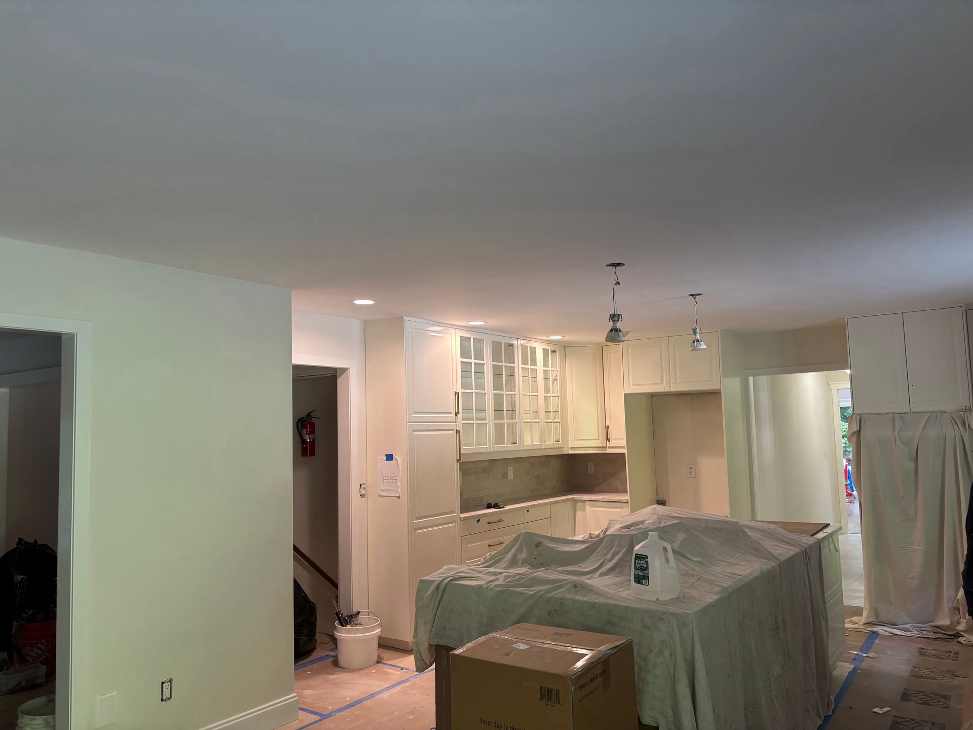 Kitchen under renovation with plastic-covered island, white cabinets, and stainless steel refrigerator
