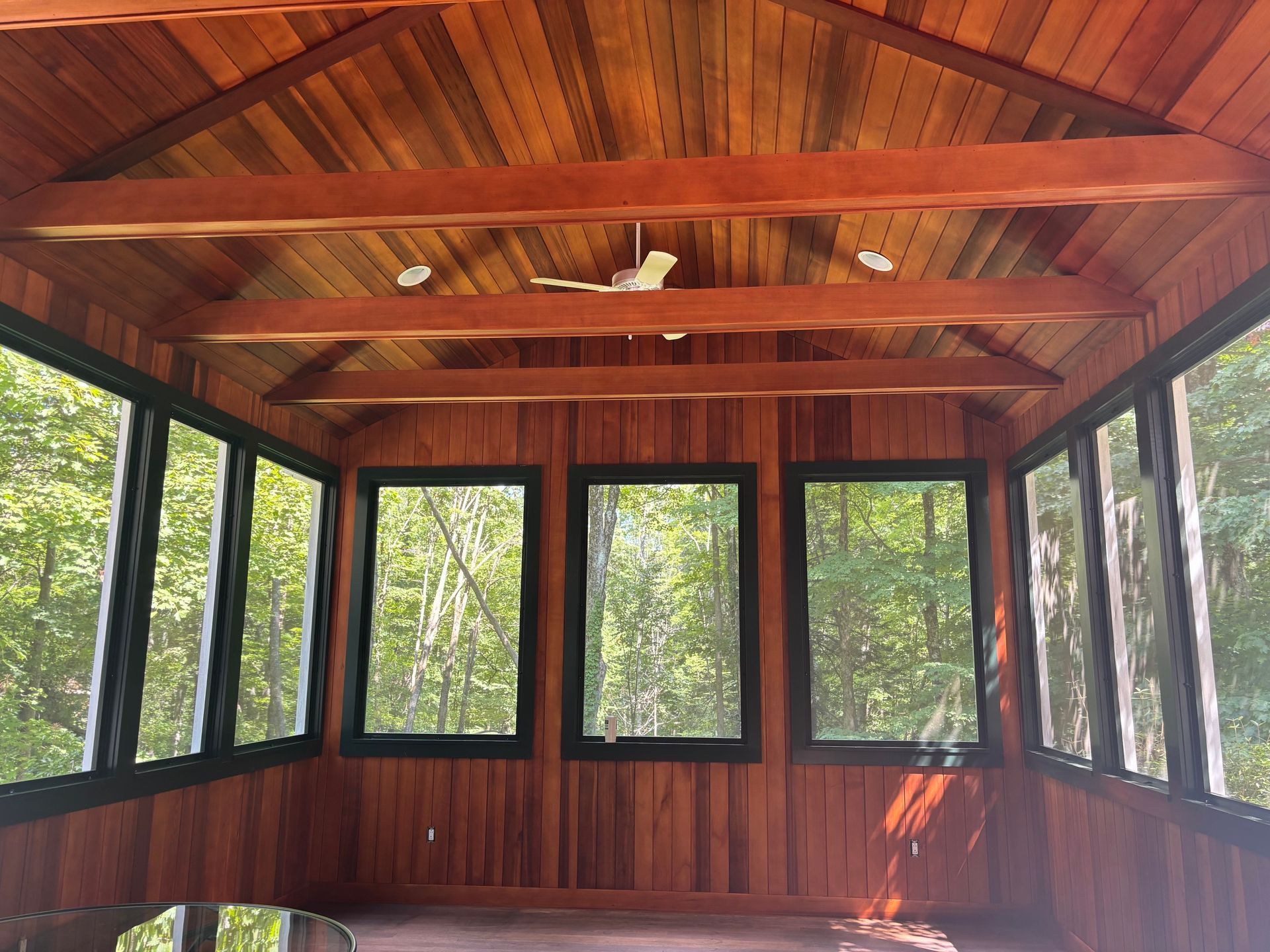Wood-paneled sunroom with large windows, a vaulted ceiling, and trees visible outside