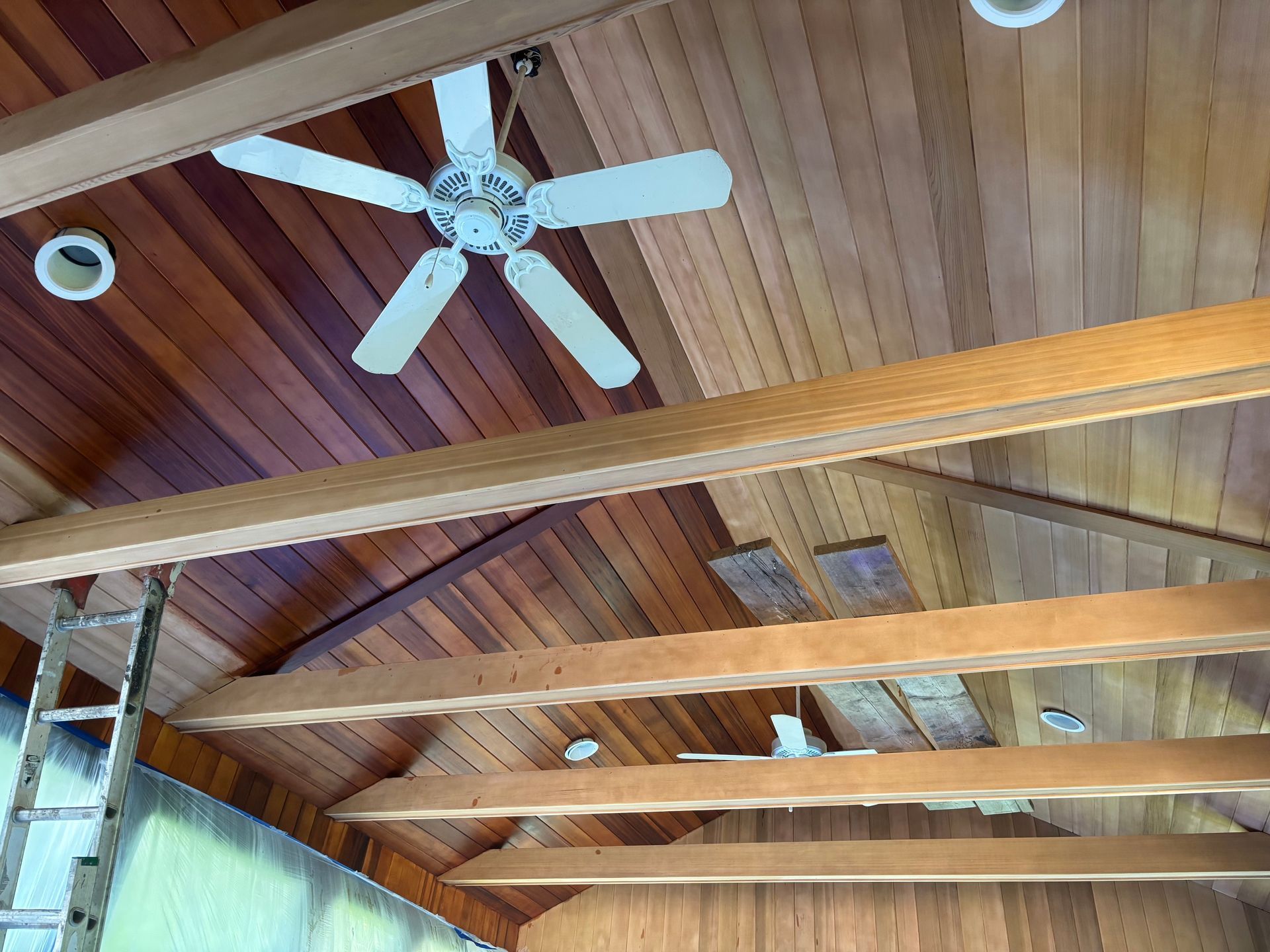 Wood-paneled vaulted ceiling with exposed beams, white ceiling fan, and recessed lights