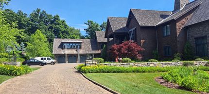 Large brick house with gabled roof, driveway, and landscaped front yard on a sunny day