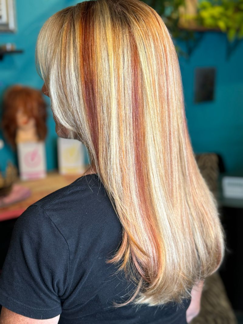 A woman with long blonde hair and red highlights is wearing a black shirt.