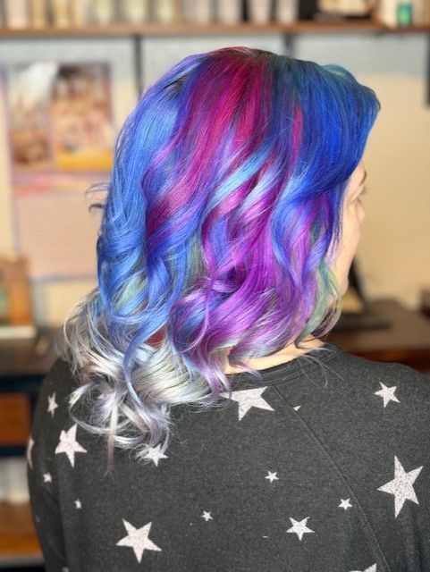 A woman with blue and purple hair is wearing a black sweater with stars on it.