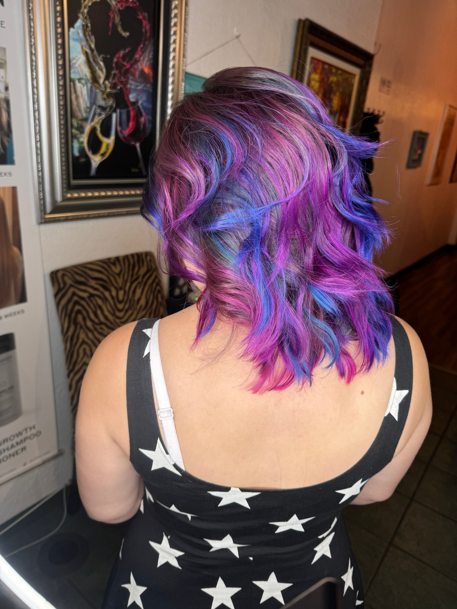 Woman with vibrant purple and blue hair, wearing a black dress with white stars, in a gallery.