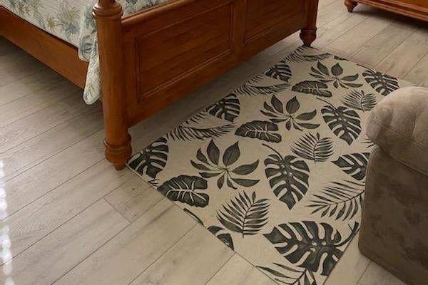 A rectangular area rug with a dark green tropical leaf pattern on a light background, placed on a light wood floor.